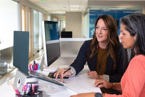 female-manager-talking-colleague-desk